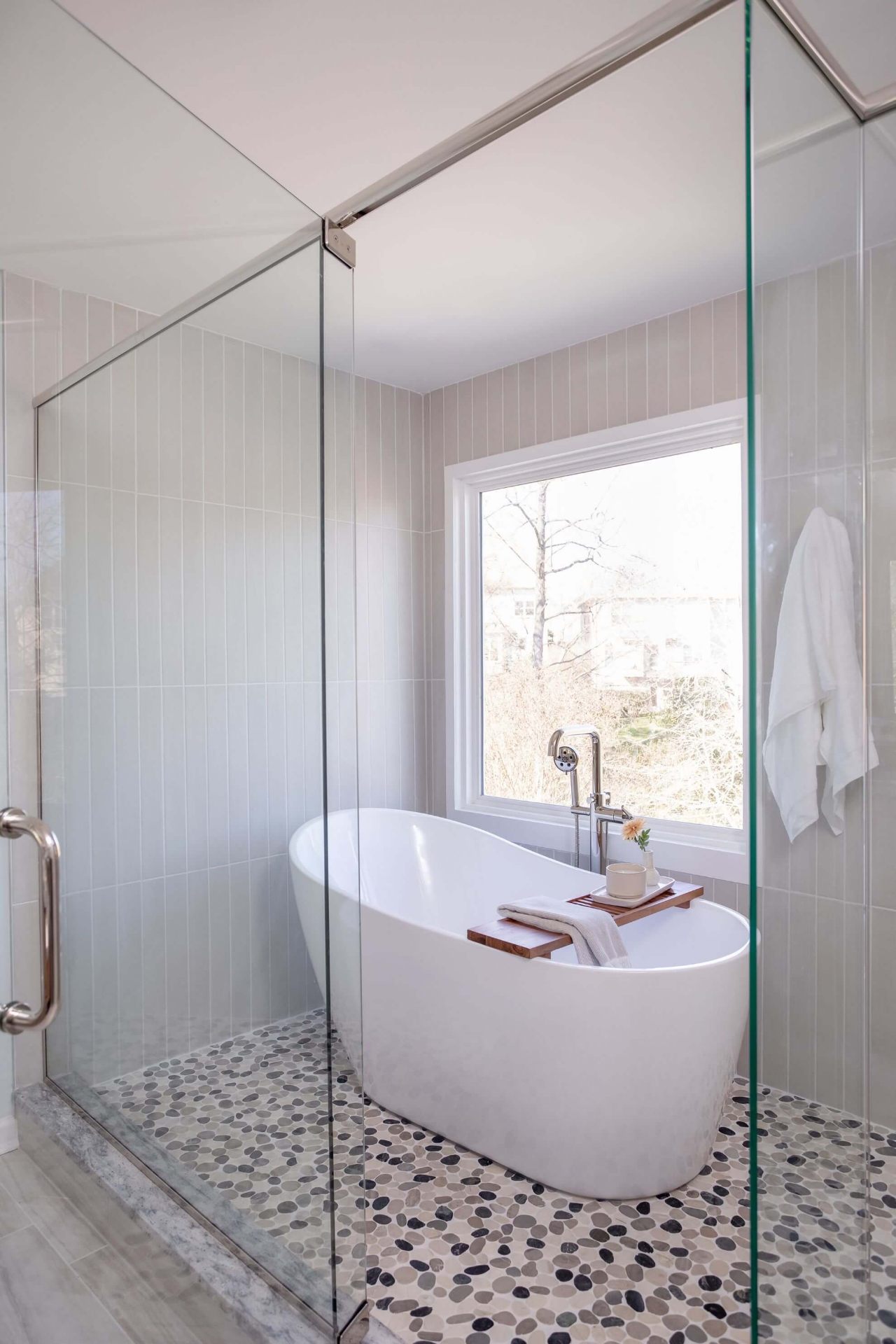 Luxury Cary bathroom with freestanding tub inside glass enclosure, pebble tile flooring, and natural light from picture window