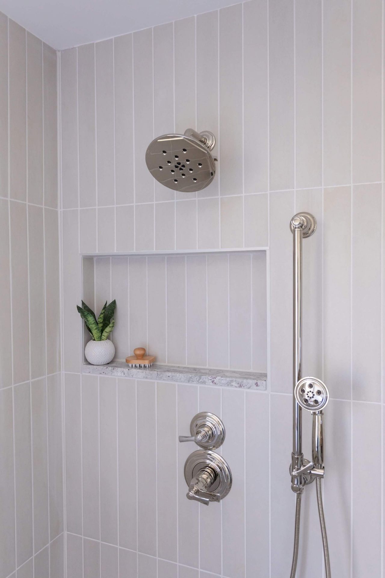 Custom shower remodel featuring vertical subway tile, polished nickel rain showerhead, marble shelf niche, and handheld shower wand