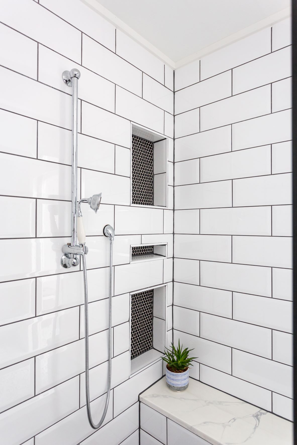 Fuquay-Varina master shower featuring white subway tile walls, triple recessed niches with black penny tile accent, chrome slide bar, and marble bench seat