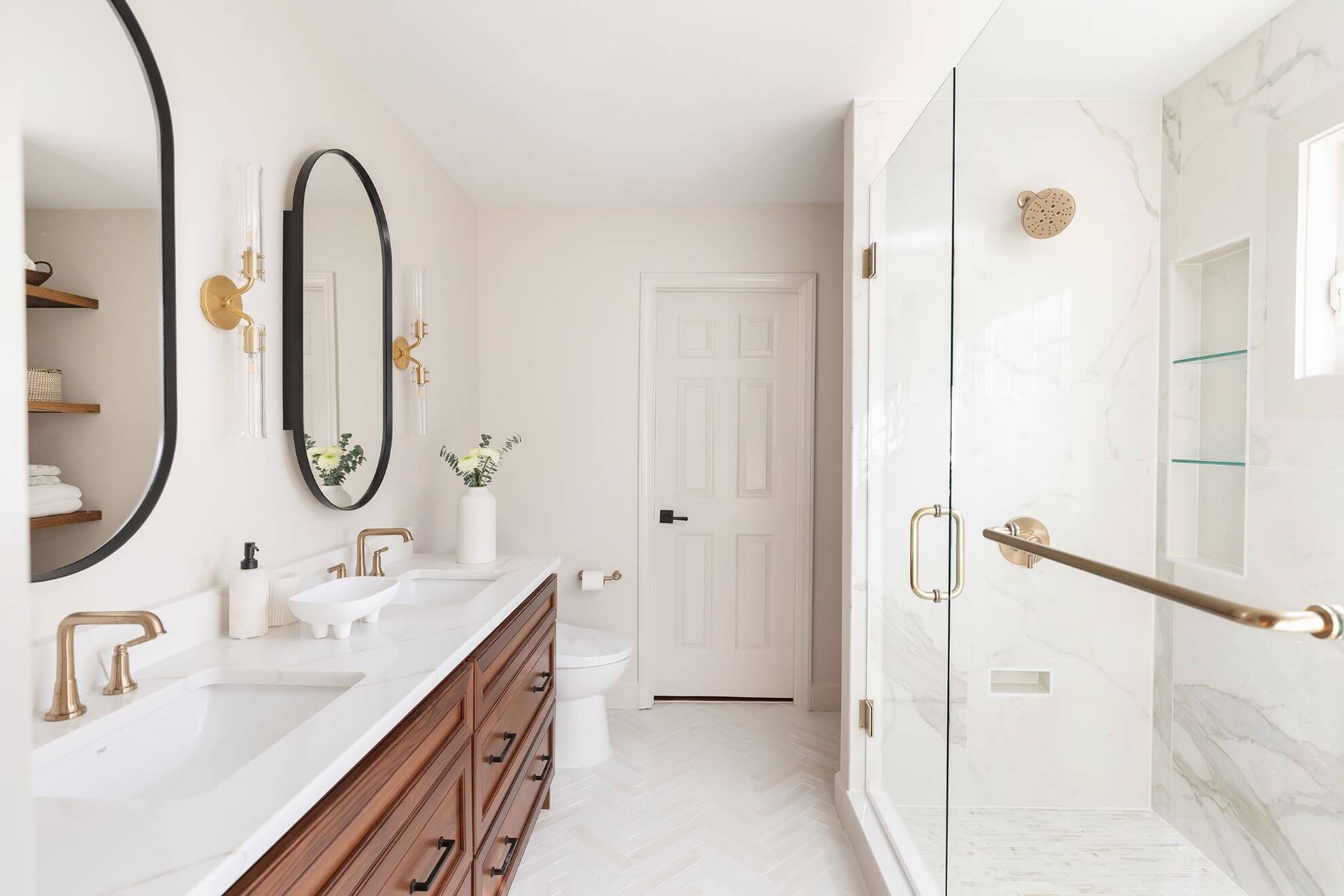 Complete Morrisville master bathroom remodel with walnut double vanity, herringbone tile floor, marble shower, and champagne gold fixtures
