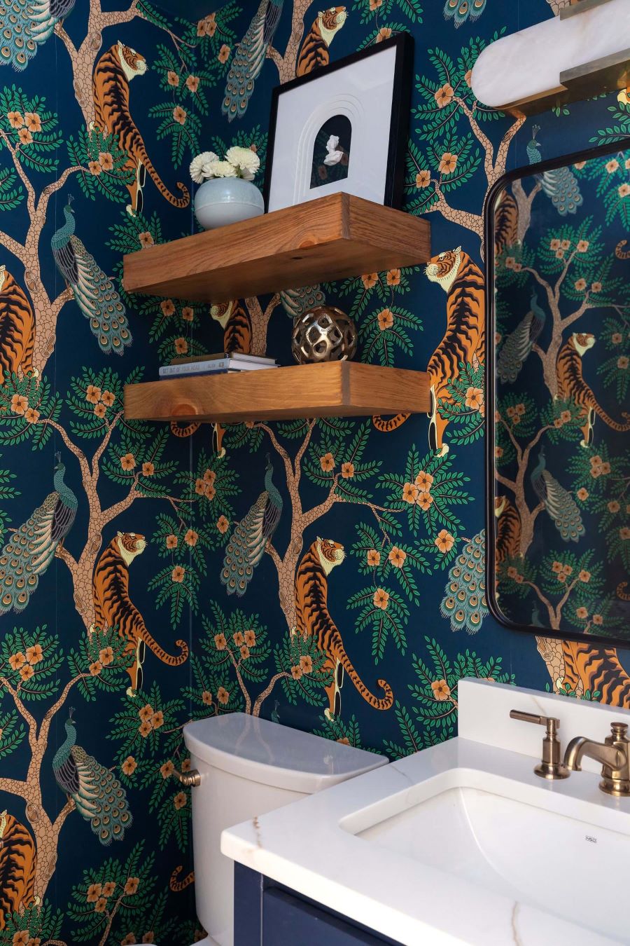 Statement Morrisville powder room with bold tiger and peacock wallpaper, floating wood shelves, navy vanity, and antique brass faucet