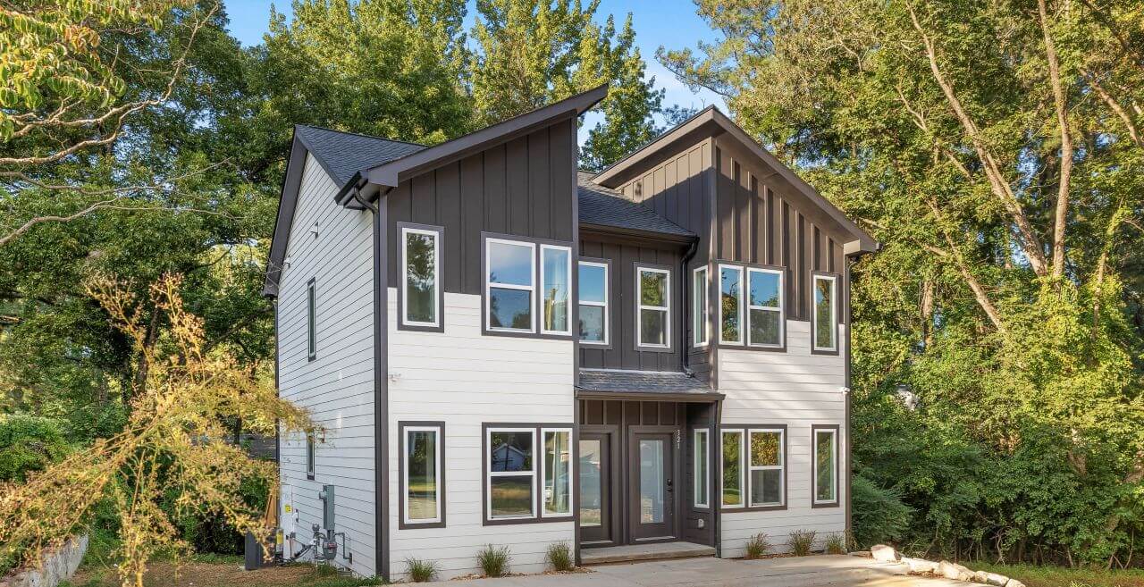 Fuquay-Varina two-story duplex with dark charcoal and white siding, modern angular architecture, large windows, and wooded lot