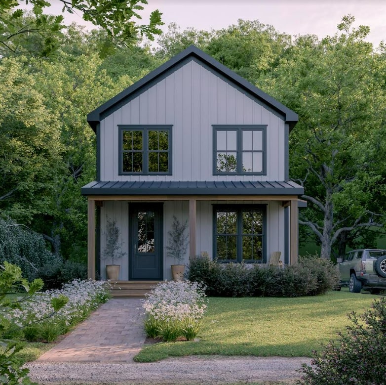 Two-story starter home with white board-and-batten siding, charcoal metal roof, covered front porch with wood posts, black-framed windows, brick paver walkway, and lush landscaping in Triangle NC
