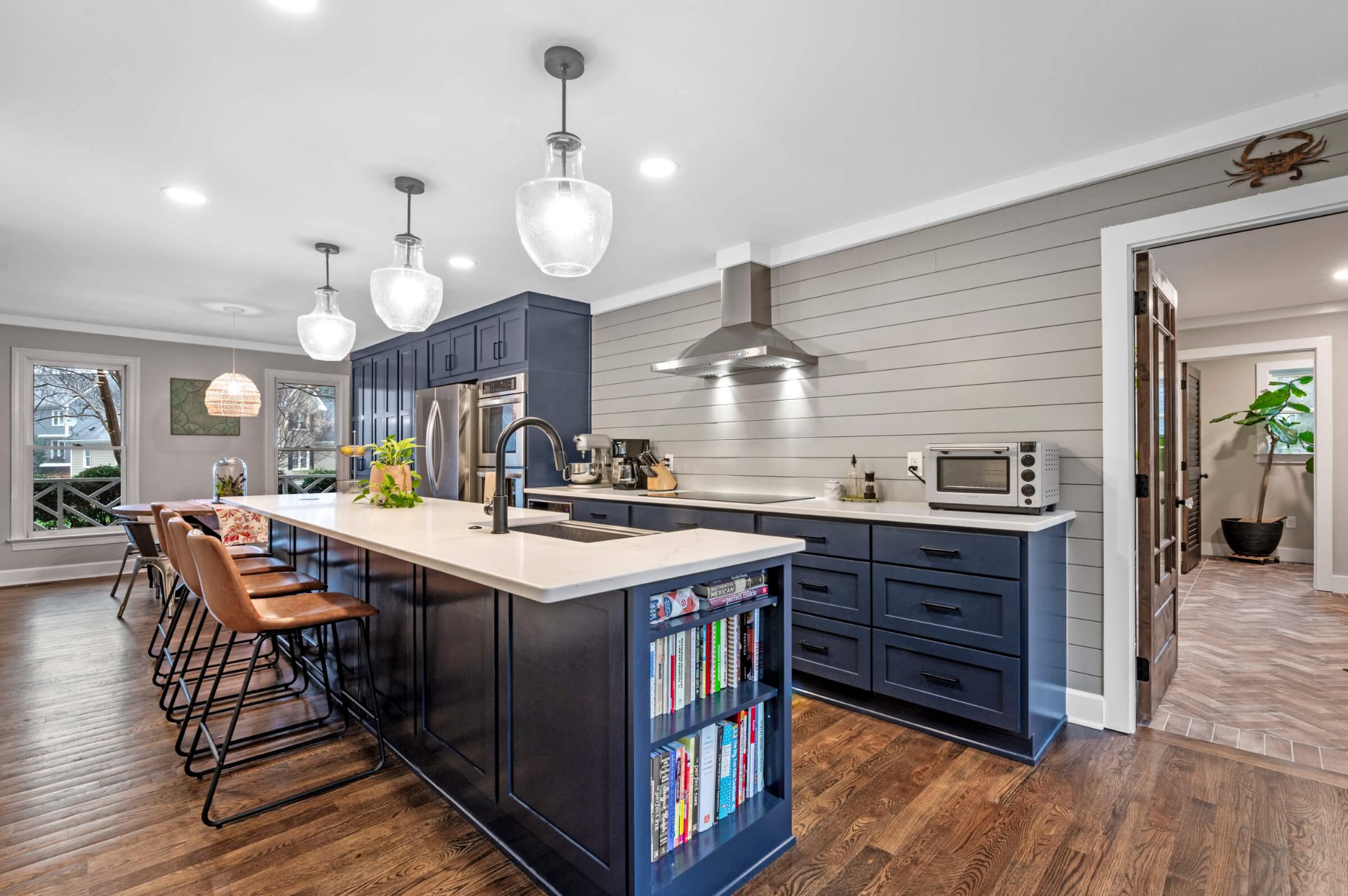 Open concept Apex kitchen renovation with large island, leather bar stools, and navy cabinetry with white quartz countertops