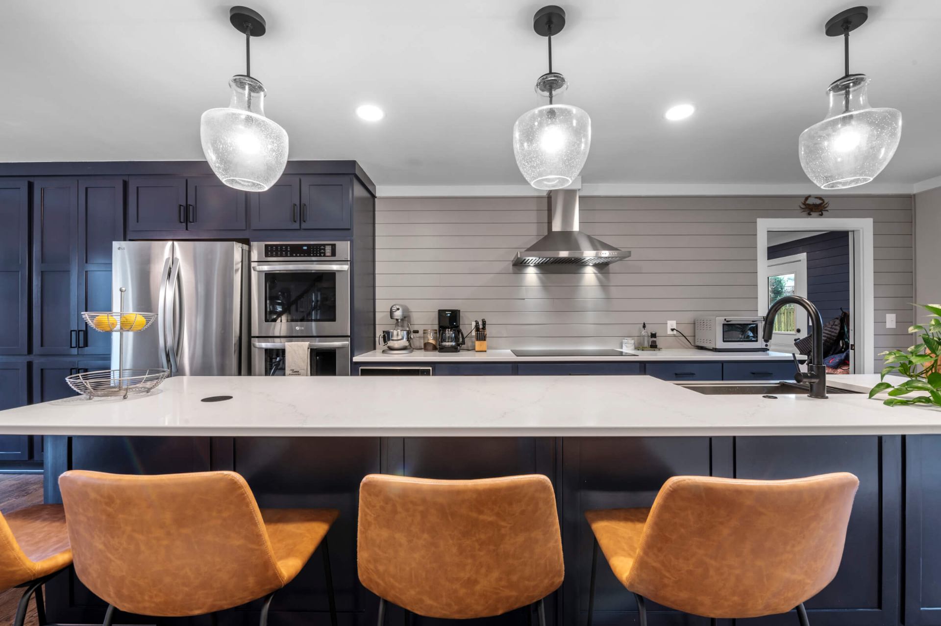 Apex kitchen island view showcasing glass pendant lights, quartz countertop, and cognac leather bar stools