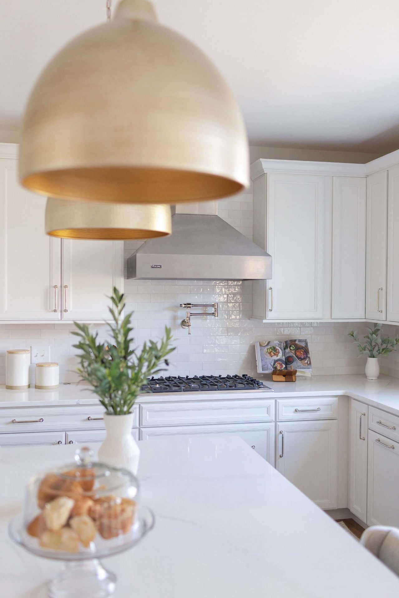 Elegant Cary kitchen featuring oversized brass pendant lights, Viking range hood, and white subway tile backsplash