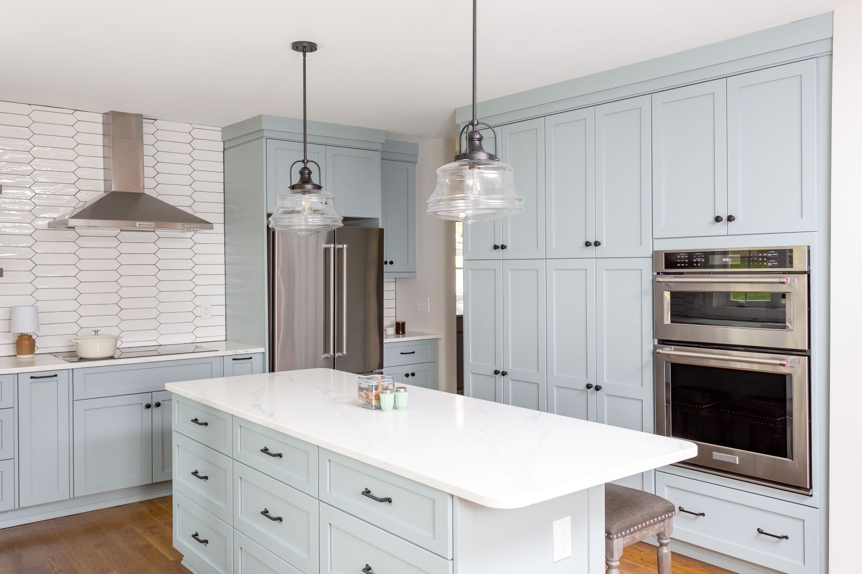 Fuquay-Varina custom kitchen with light blue shaker cabinets, white quartz island countertop, glass pendant lights, and stainless double wall oven