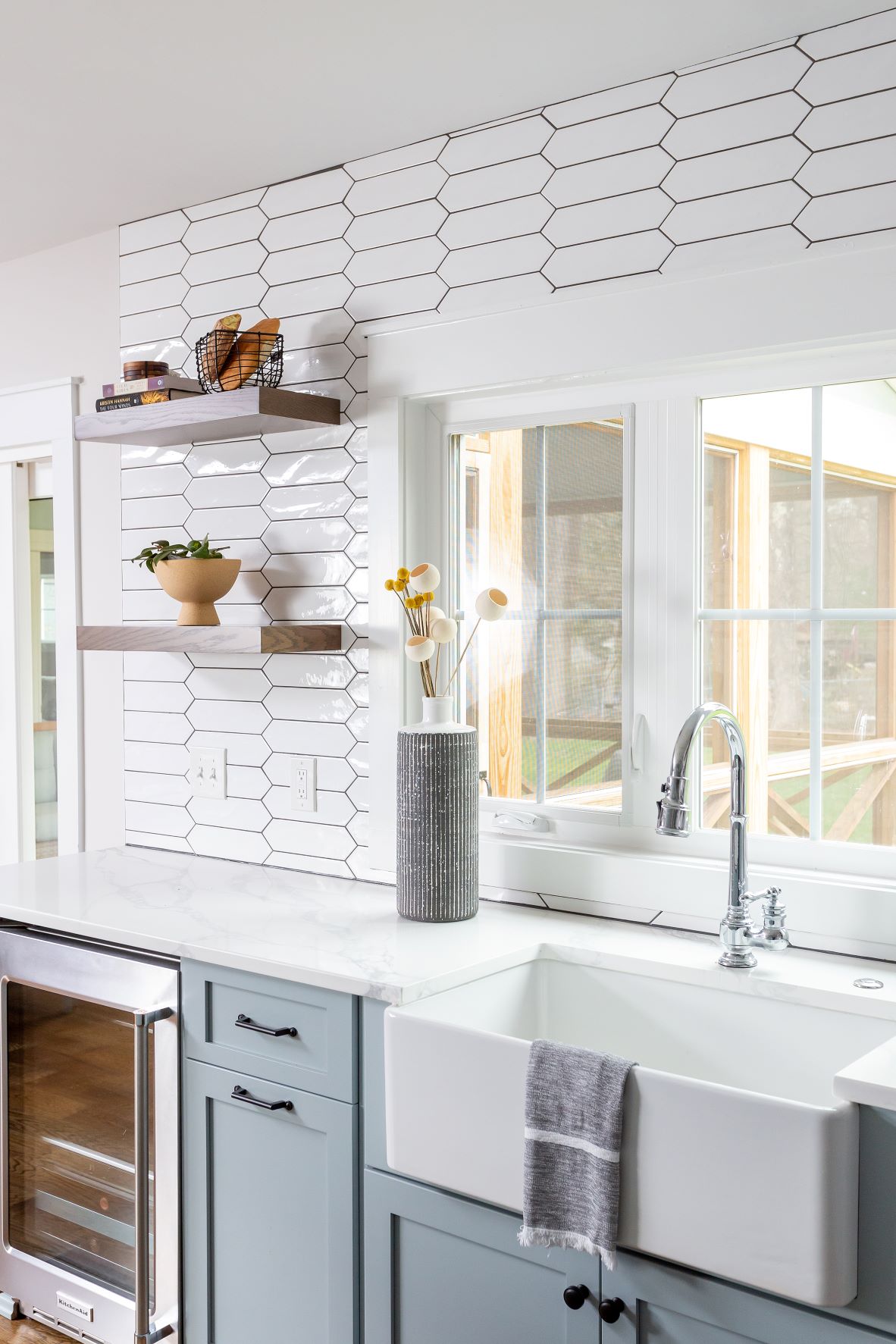 Fuquay-Varina kitchen sink station with white farmhouse apron sink, chrome bridge faucet, picket tile backsplash, and wood floating shelves
