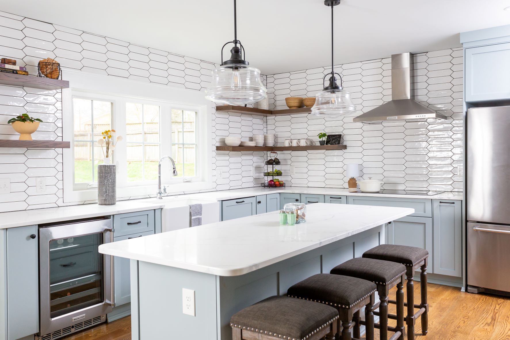 Open concept Fuquay-Varina kitchen featuring floor-to-ceiling hexagon tile backsplash, floating wood shelves, blue cabinets, and upholstered bar stools