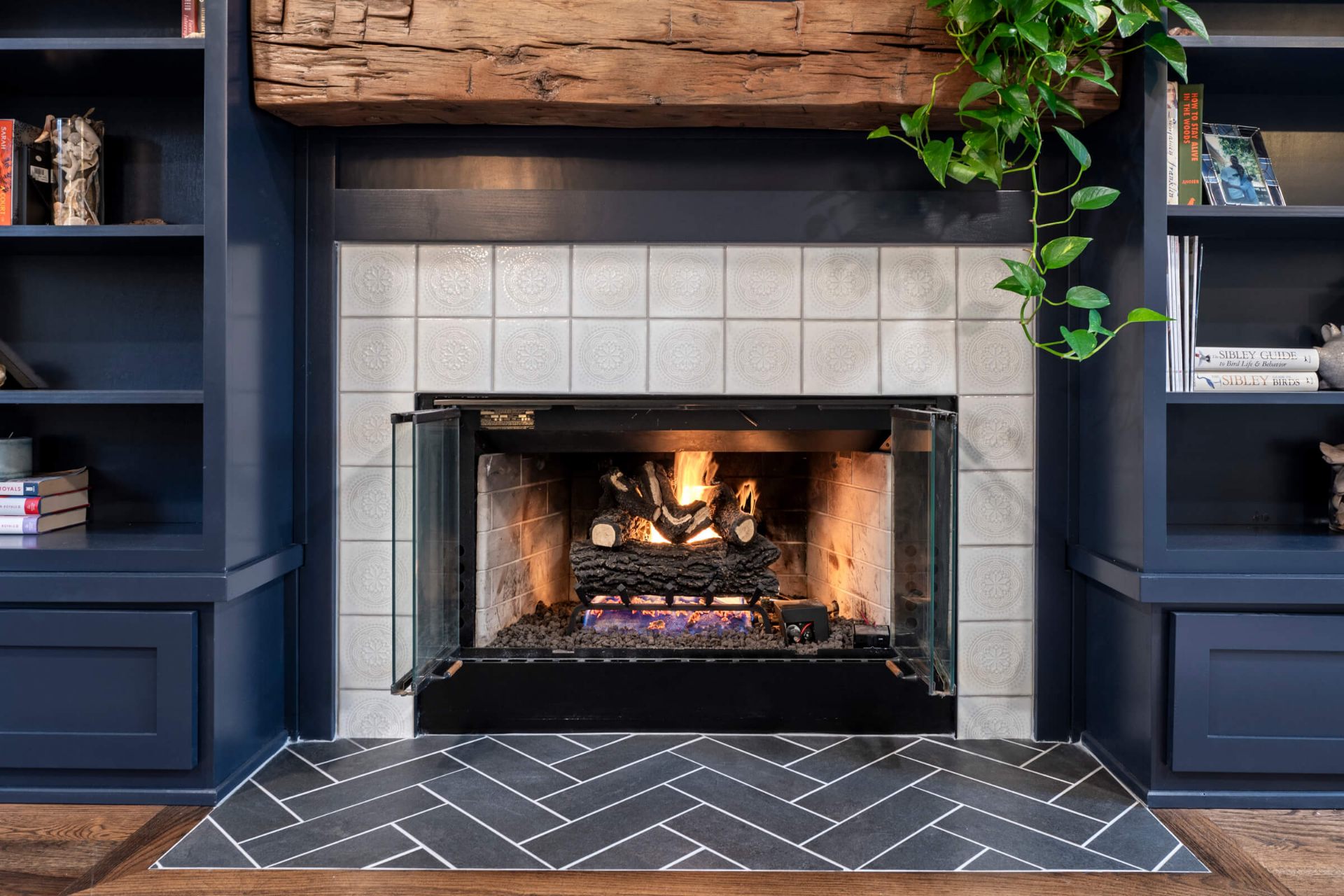 Custom fireplace renovation with decorative tile surround, reclaimed barn beam mantel, herringbone slate hearth, and navy built-ins