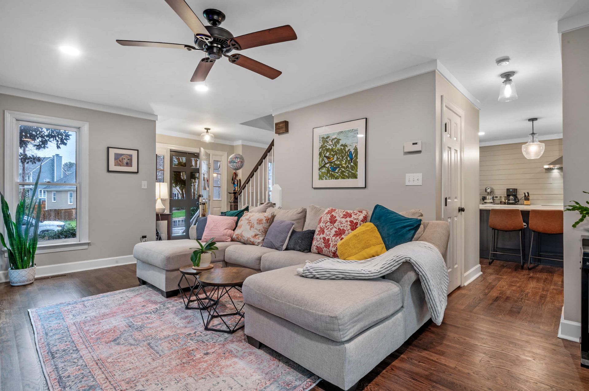 Open floor plan Apex living room with sectional sofa, ceiling fan, hardwood floors, and kitchen bar seating in background