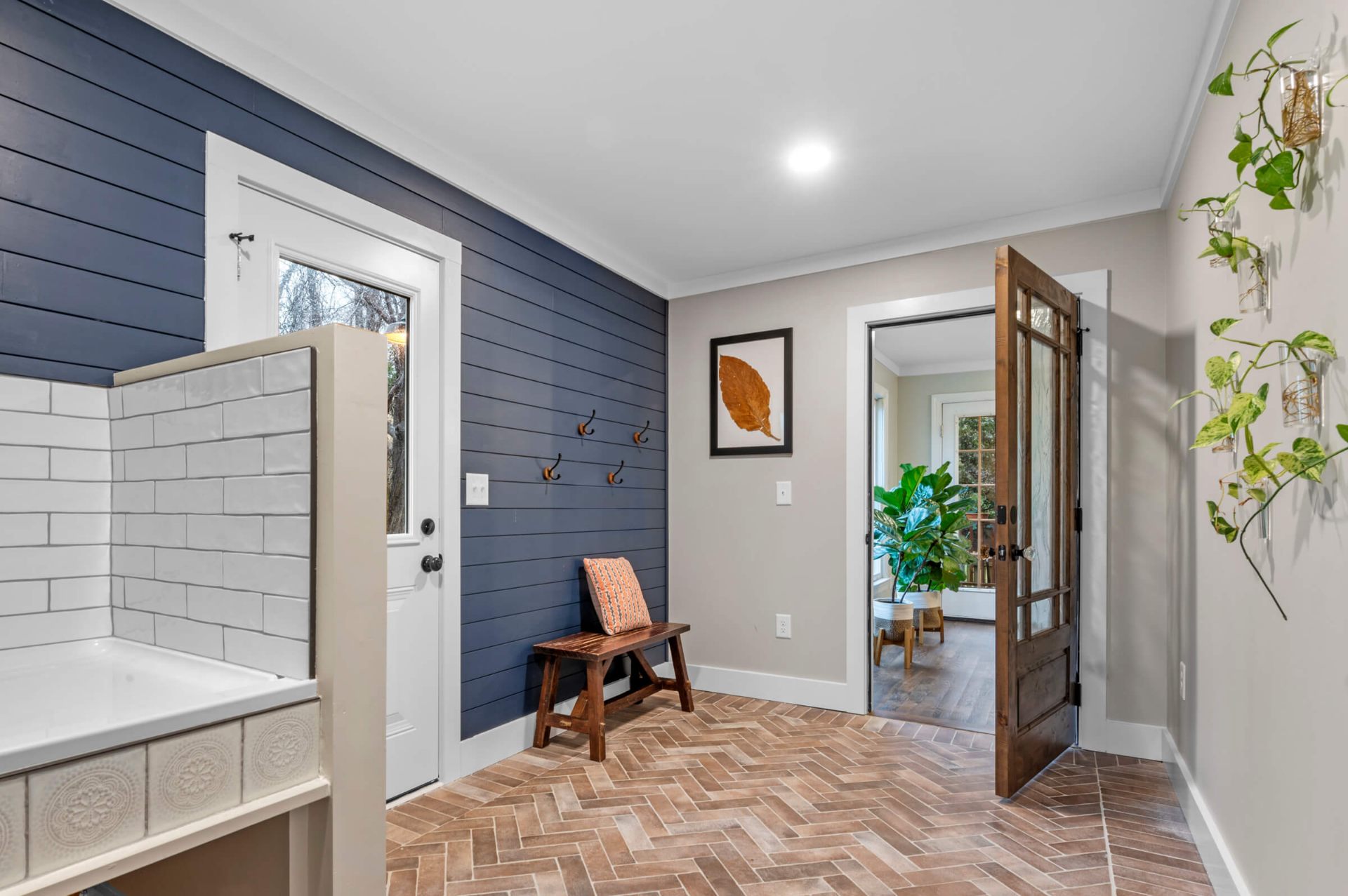 Functional Apex mudroom with blue shiplap walls, subway tile laundry station, herringbone floor, and French door to living space