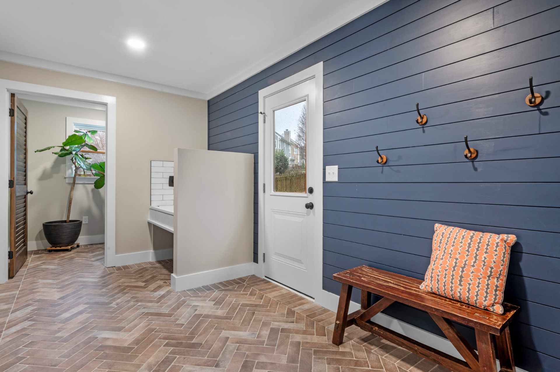 Apex mudroom renovation featuring navy blue shiplap accent wall, herringbone brick tile flooring, rustic bench, and coat hooks