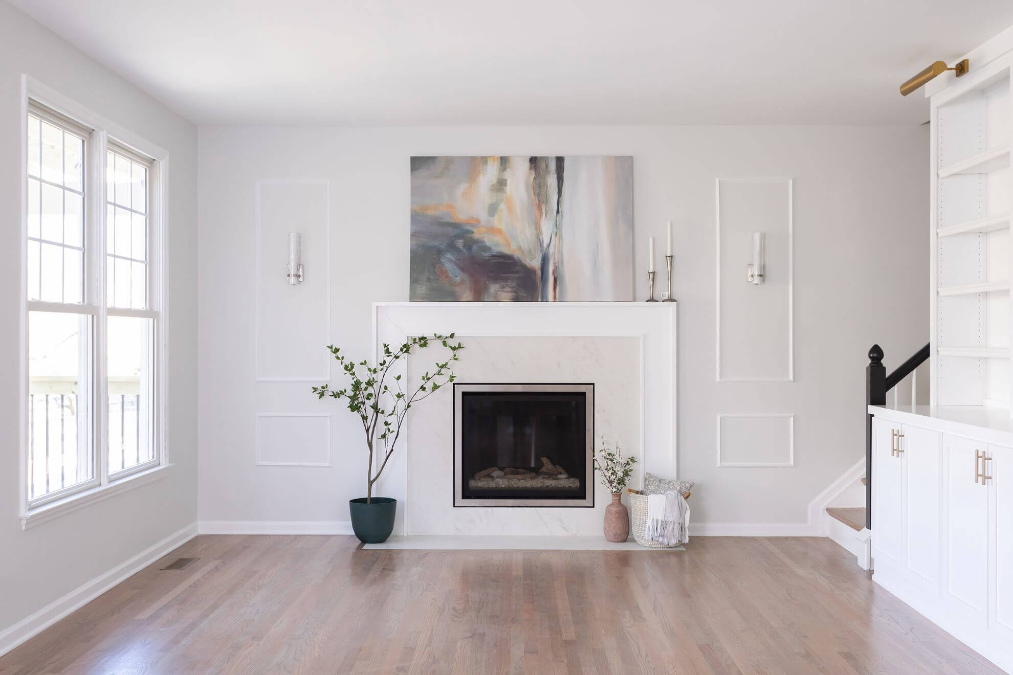 Contemporary Cary living room with white marble fireplace surround, abstract art, wainscoting panels, and light hardwood flooring
