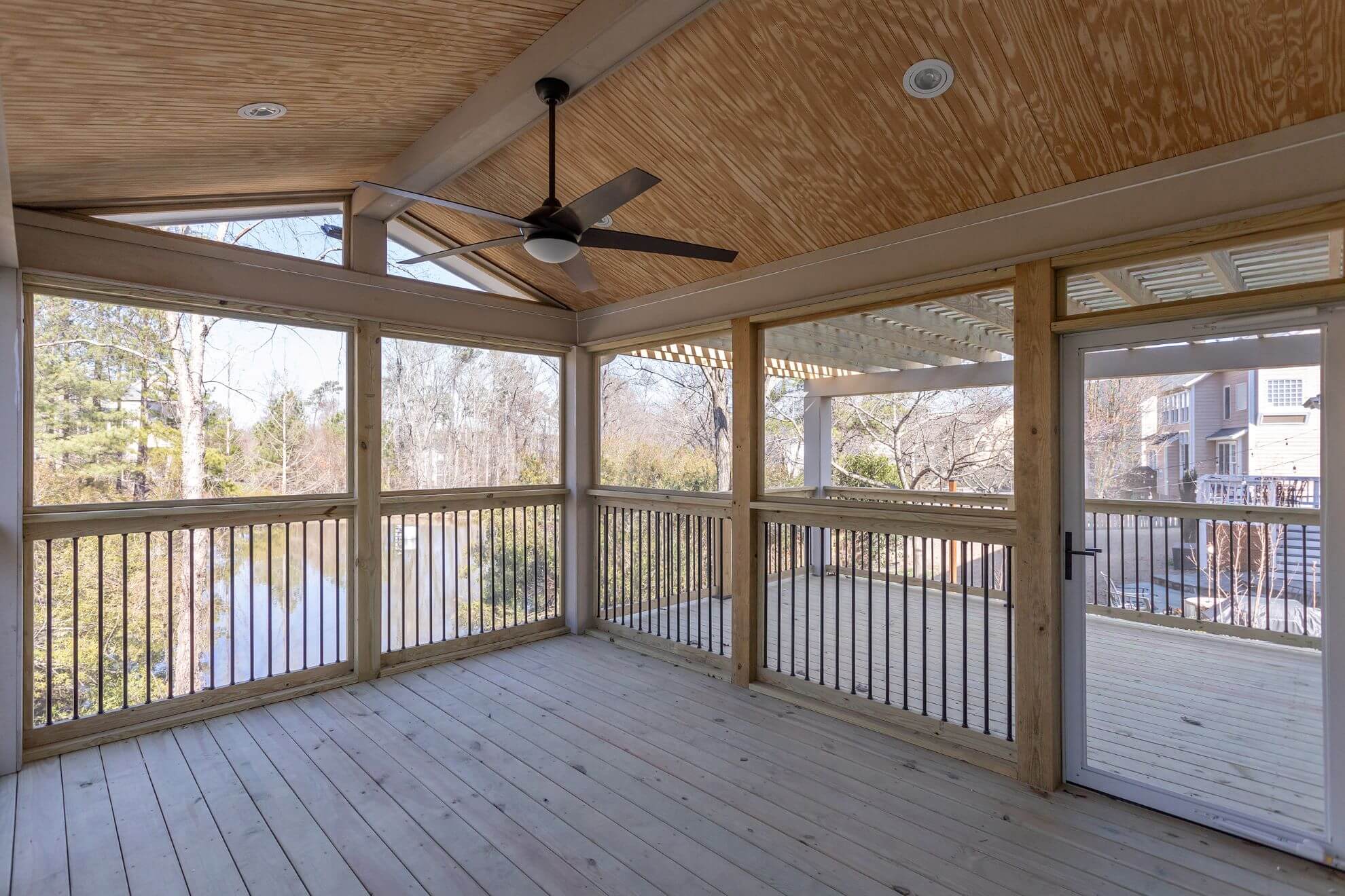 Cary screened porch addition with natural wood vaulted ceiling, ceiling fan, metal balusters, and views of wooded backyard
