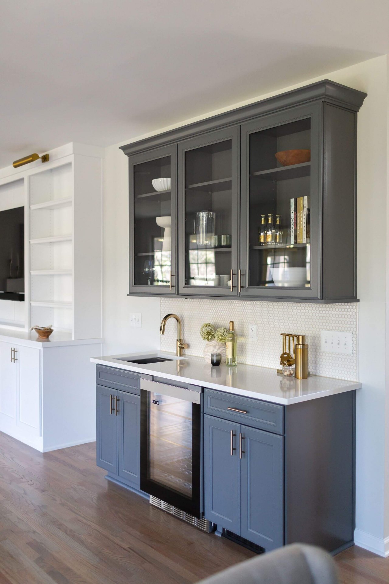 Elegant Cary wet bar with gray cabinets, glass upper cabinets, honeycomb backsplash, brass faucet, and built-in wine refrigerator
