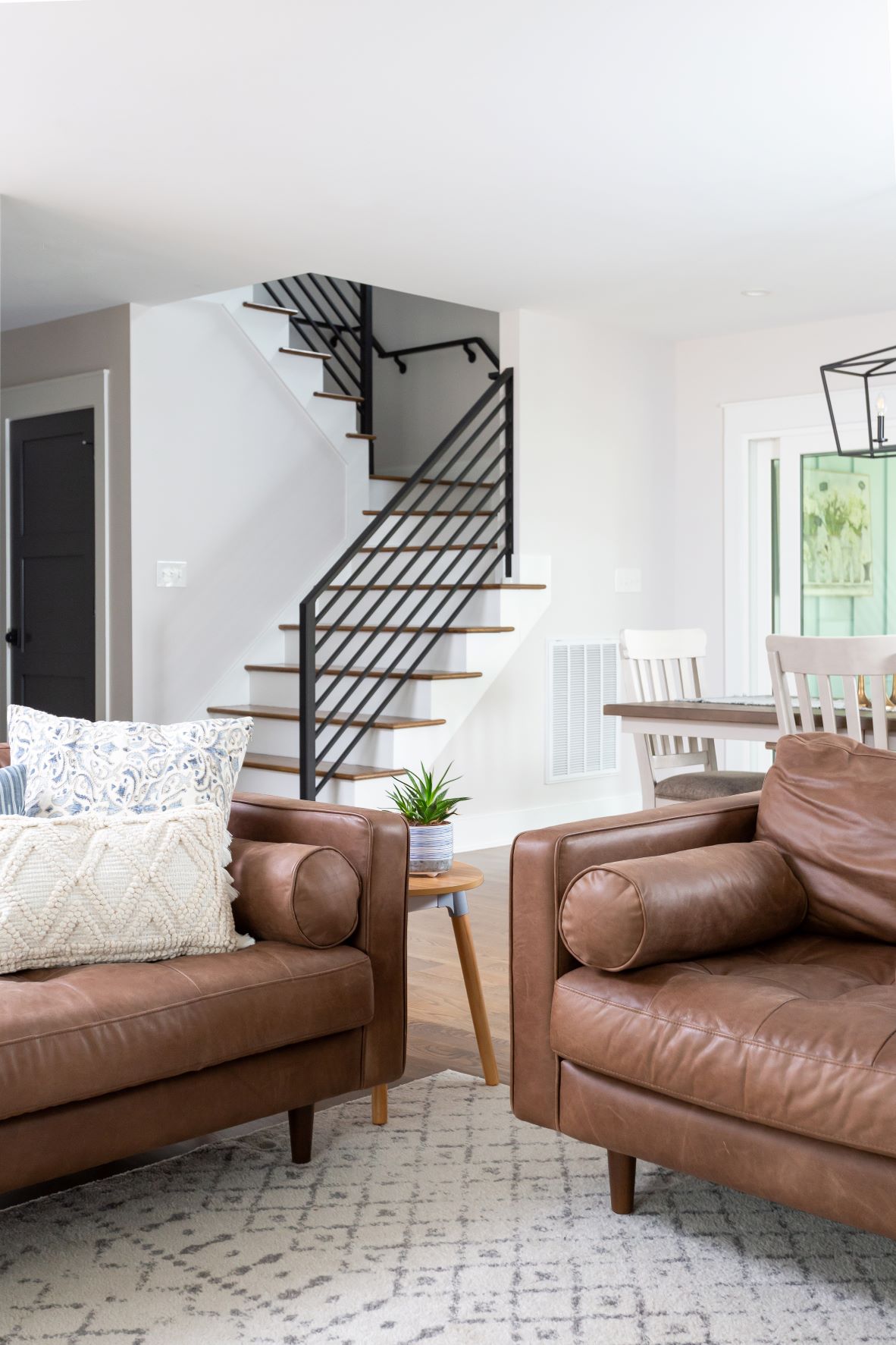 Open floor plan featuring custom floating staircase with horizontal black metal railing, oak treads, leather armchairs, and dining area