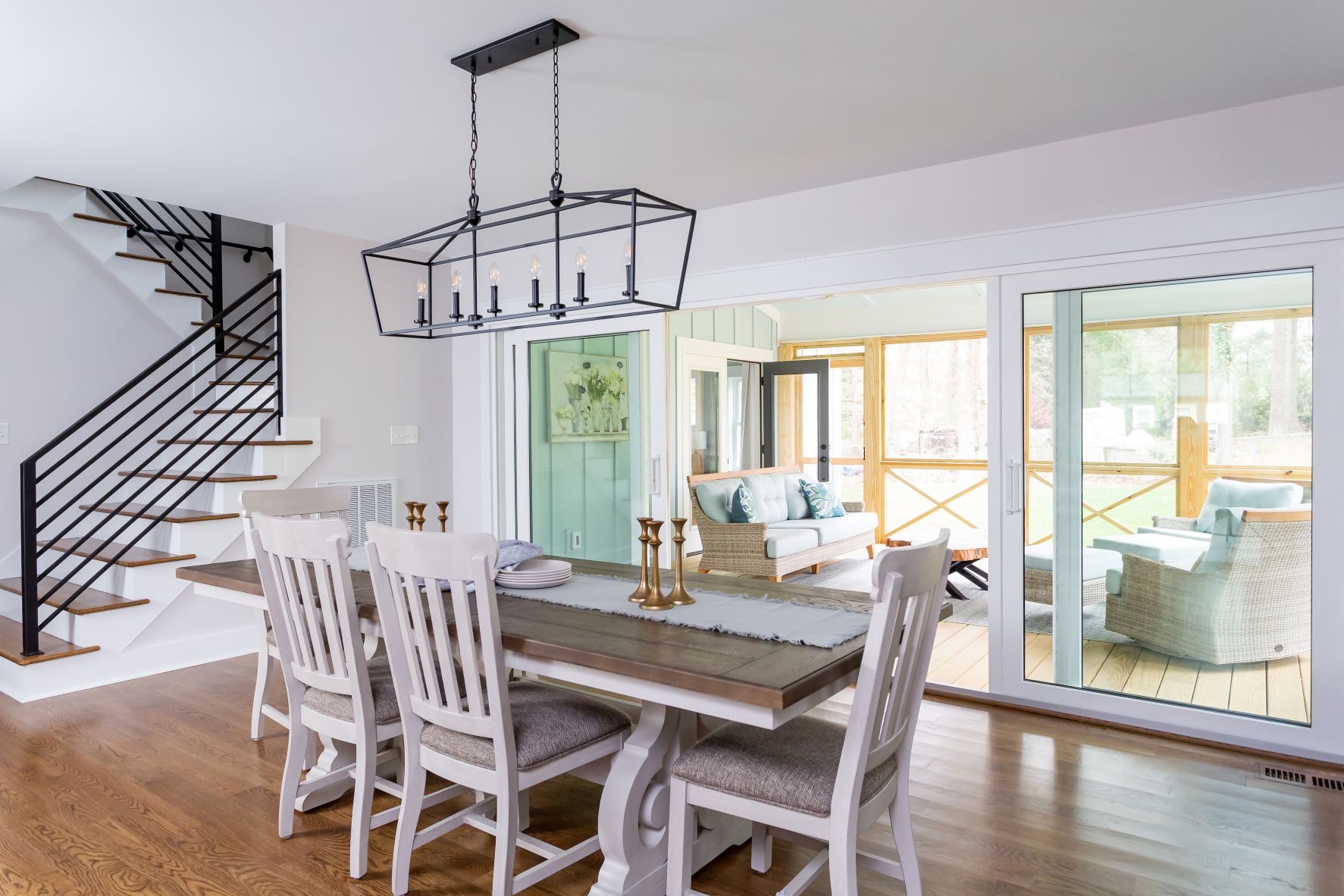 Fuquay-Varina dining room with farmhouse table, cage chandelier, modern staircase, and sliding doors to screened porch outdoor living space
