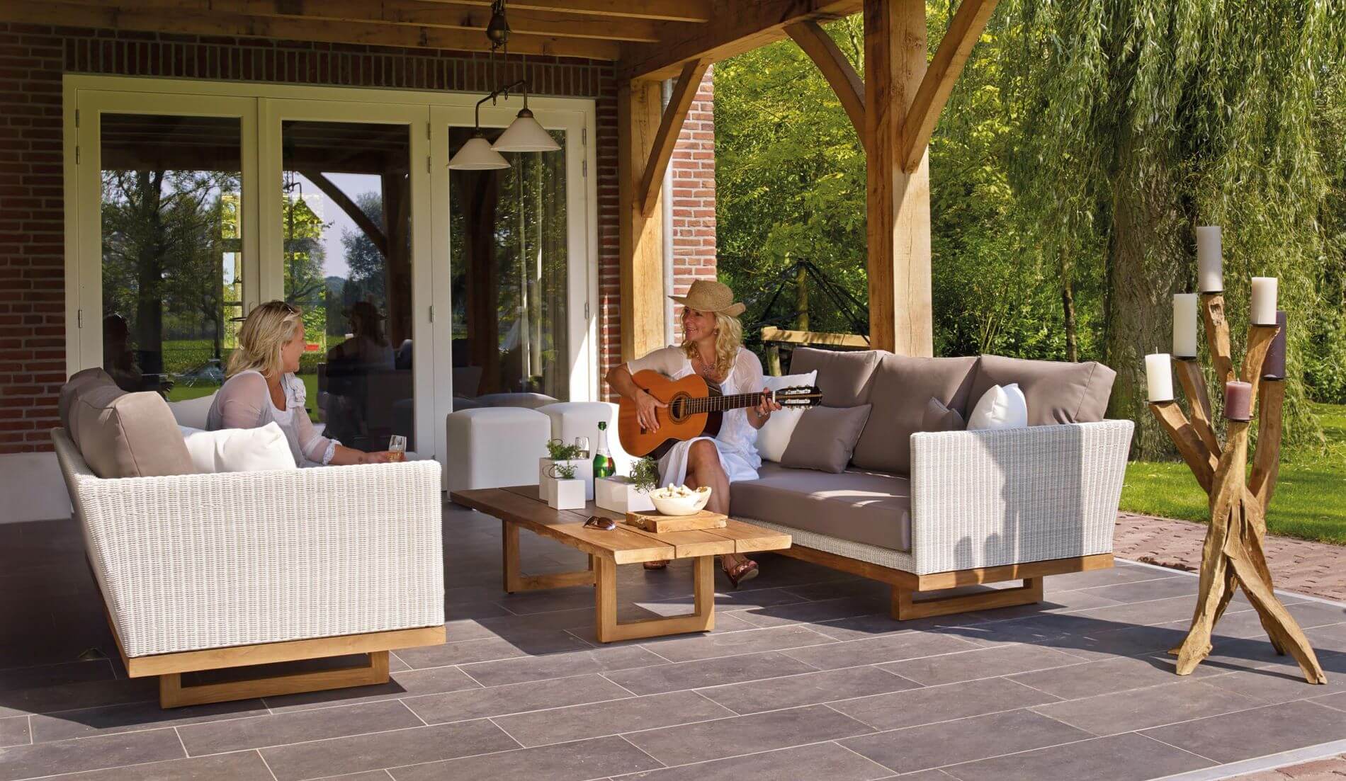 two woman sitting in outdoor living space; one woman plays guitar
